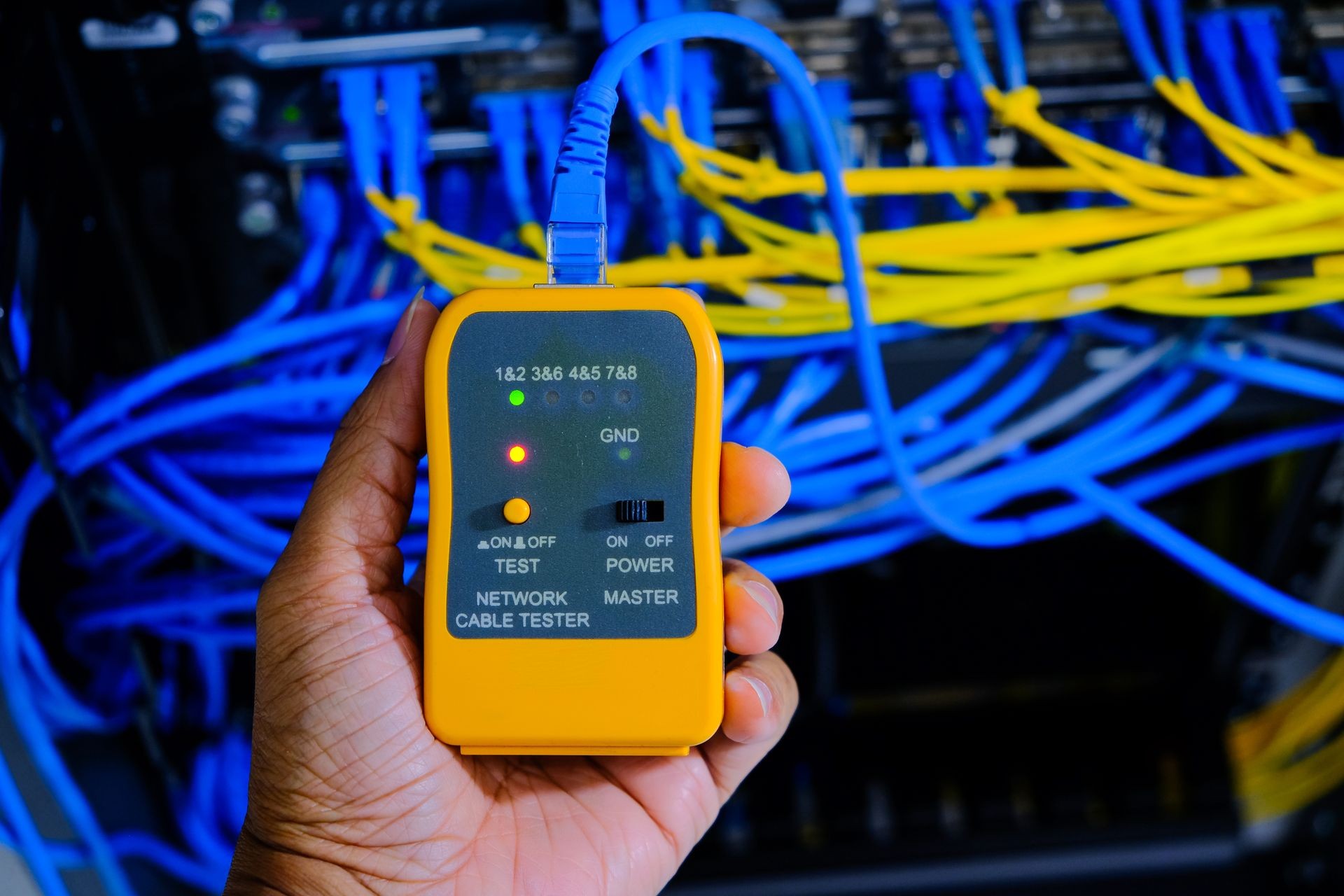 hand of system administrator or technician with tester tool for test network cables connected to patch panel of network gigabit switch in network data center